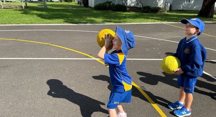 Two students taking turns to shoot hoops on the basketball court