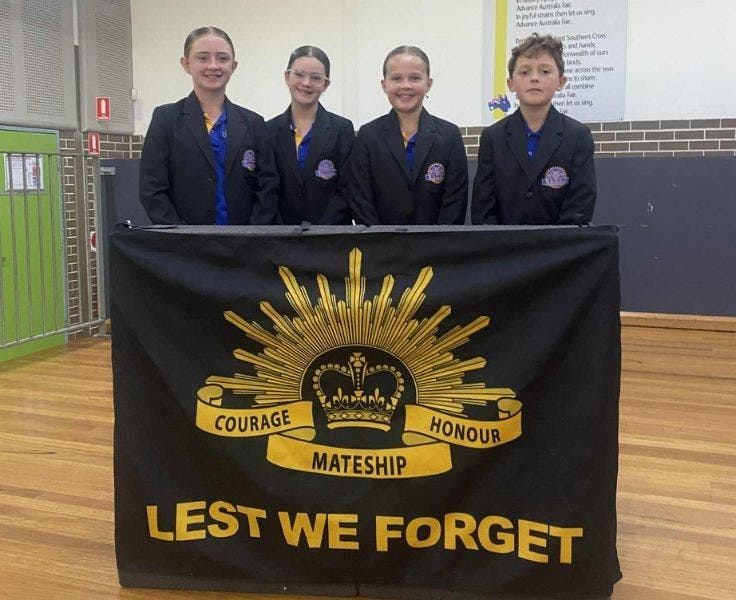 Four students standing behind a Lest We Forget banner